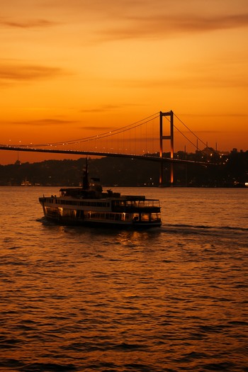 Gün batımında köprü ışıkları ve Boğaz’dan geçen vapur silüeti